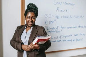 A teacher holding books standing in front of her whiteboard in a classroom