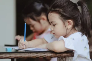 A young girl writing with a pencil in a classroom