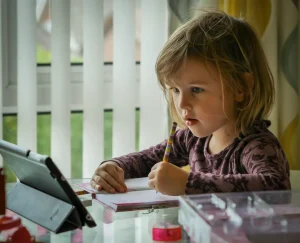 A young girl reading off an Ipad whilst writing