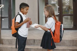 Two students talking outside of a school with backpacks