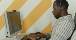 A man sat at his laptop typing whilst wearing headphones