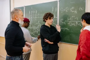 A lecturer standing with his students at a blackboard working out a complicated problem together