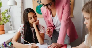 A female teacher helping two students with their work at a table