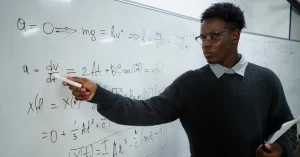 A male teacher writing on a whiteboard in a classroom