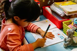 A child writing on a workbook at her desk