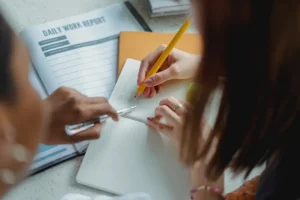 Close up of a girl writing with her teacher next to her assisting