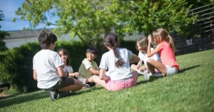 several young children sitting in a circle outside playing a game