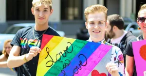 Two young men at a pride event holding a sign that says "love is love"