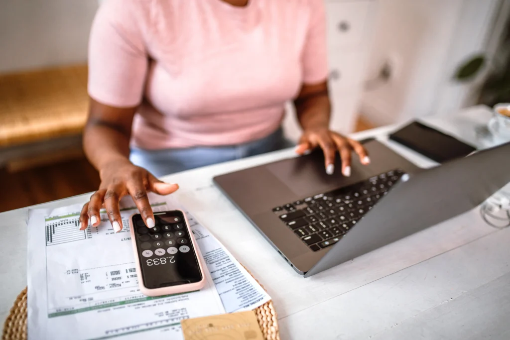 A woman on a laptop and calculator working out her household budget